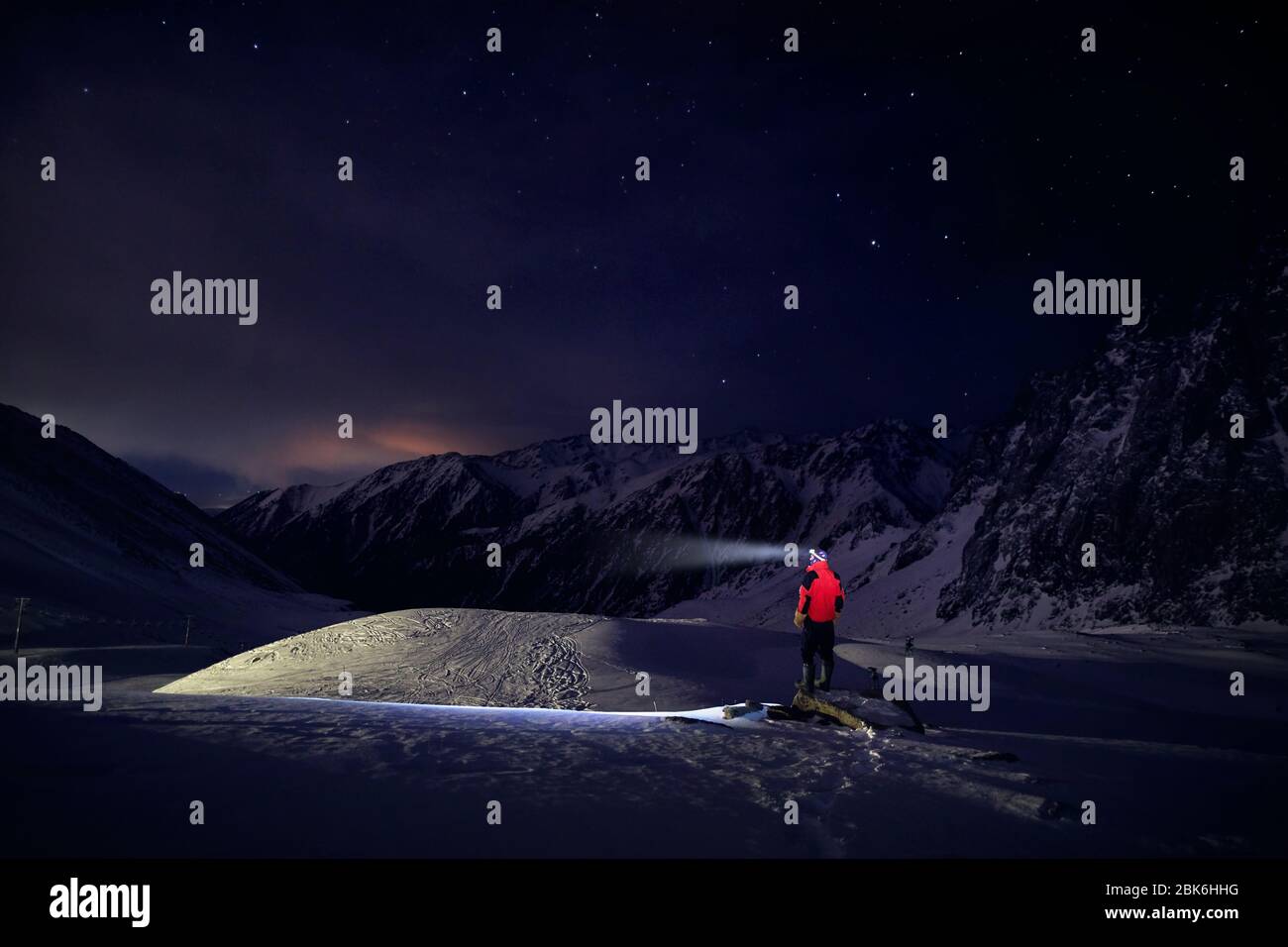 Mann im roten Mantel mit Ray von seinem Kopf Licht am sternenklaren Nacht den Berg im Skigebiet im Winter Stockfoto
