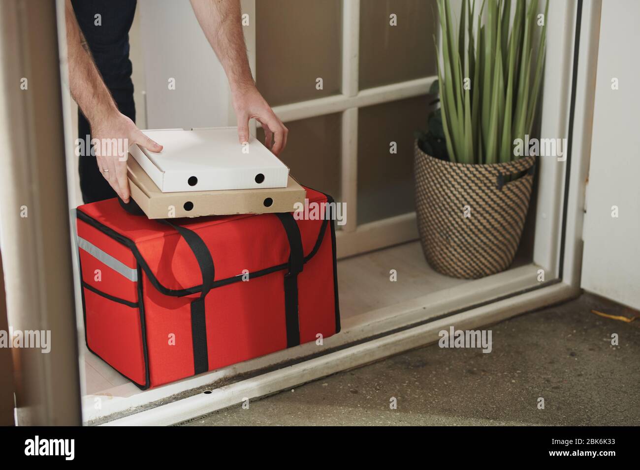 Hände kranken jungen Mannes, der zwei Kisten mit Pizza und großen roten Beutel mit Lebensmitteln an der Tür während des Aufenthalts zu Hause Stockfoto