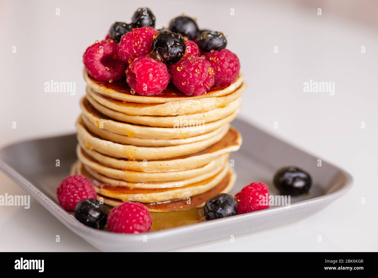 Graue quadratische Platte mit Stapel appetitlich und lecker hausgemachten Pfannkuchen mit Honig Tropfen und frischen Beeren stehen auf dem Tisch Stockfoto