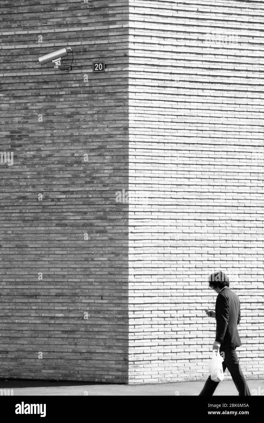 CCTV-Kamera an einer Ziegelmauer und ein Mann, der vorbei geht Stockfoto
