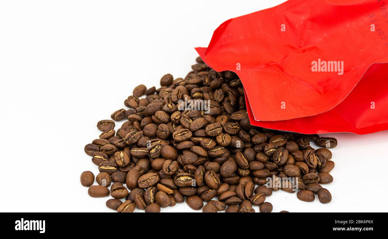 Ein roter Beutel mit frischen Kaffeebohnen wird auf einen weißen Hintergrund gegossen. Stockfoto