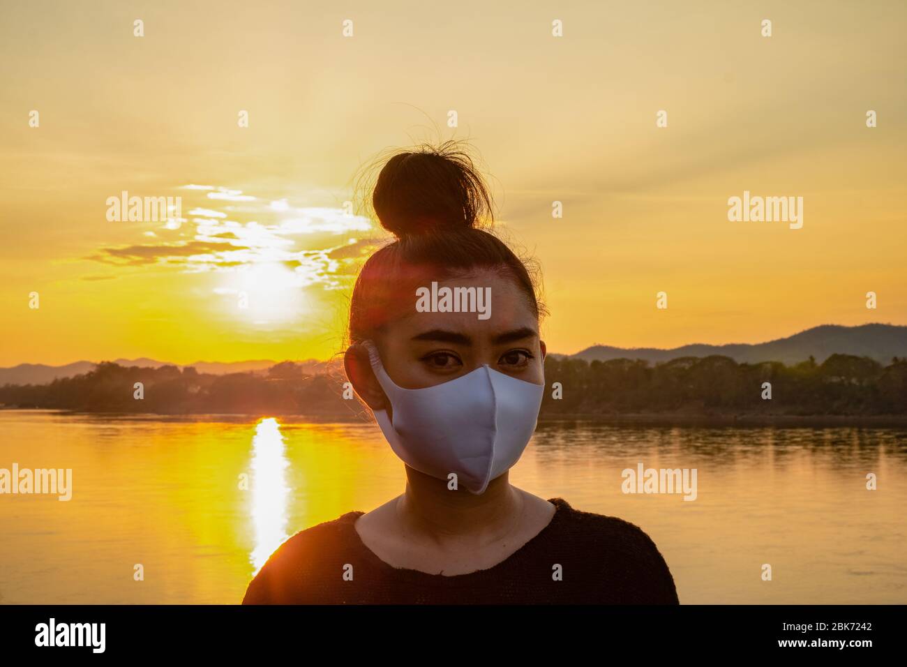 Nahaufnahme junge Asienfrau, die eine Fack Maske aufsetzt, um vor luftgetragenen Atemwegserkrankungen zu schützen, wie die Grippe-covid-19 PM2.5 Staub und Smog bei Sonnenuntergang backg Stockfoto