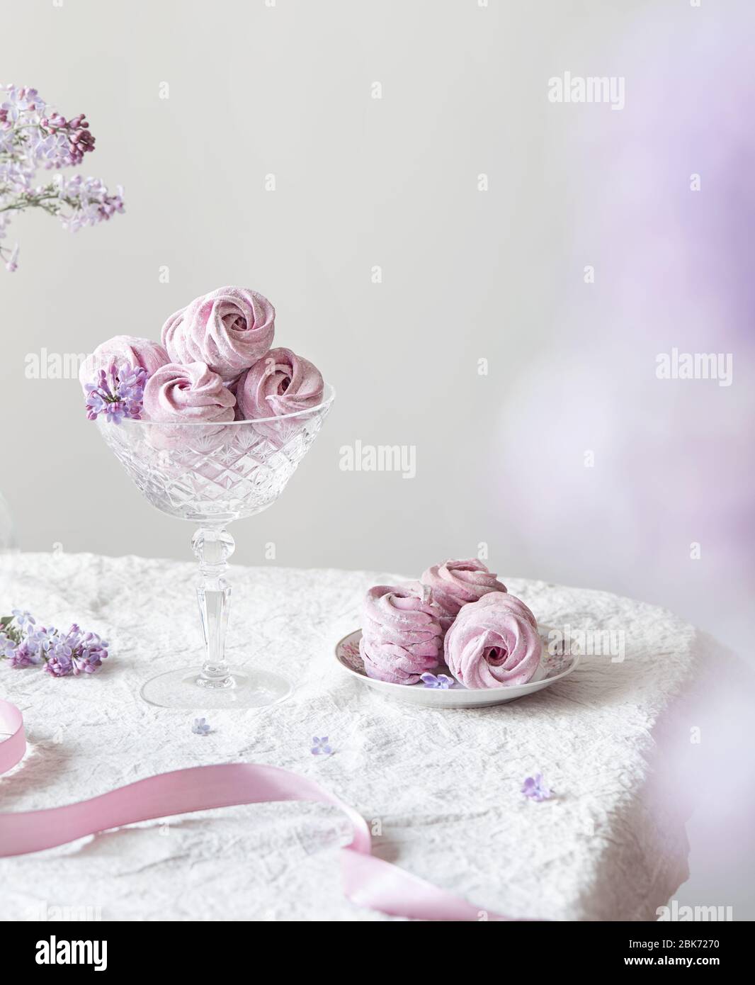 Violett süß hausgemachte Zephyr oder Marshmallow aus schwarzer Johannisbeere um lila Blüten auf weißem Tischtuch und hellen Hintergrund Stockfoto
