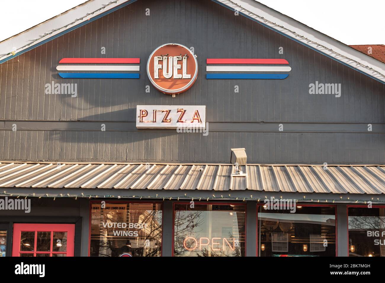 Horizontale Aufnahme der Fassade von 'Fuel Pizza' in South Charlotte, aufgenommen in der Abenddämmerung, mit Marke und Logo über Glasfenstern und Eingang des Restaurants. Stockfoto