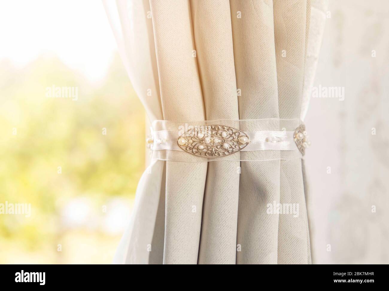 Nahaufnahme des Vorhanghalters im Innenbereich, Wohnkultur. Minimalistischer grauer Vorhang im weißen Schlafzimmer mit Sonnenlinsenflecken. Stockfoto