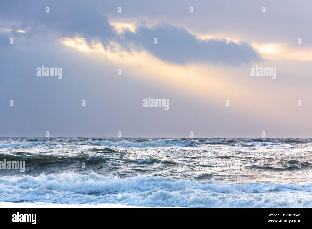 Sonnenstrahlen brechen durch dunkle Wolken über der aufwührenden Nordsee Stockfoto