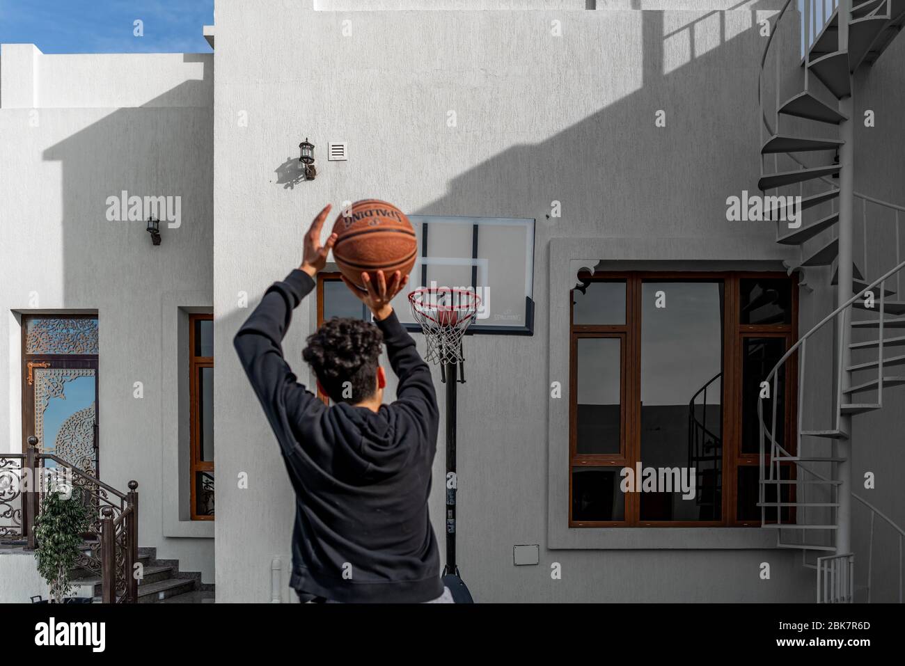 Junger Mann, der im Freien Basketball im Hinterhof spielt und einen Ball am Rand schießt Stockfoto