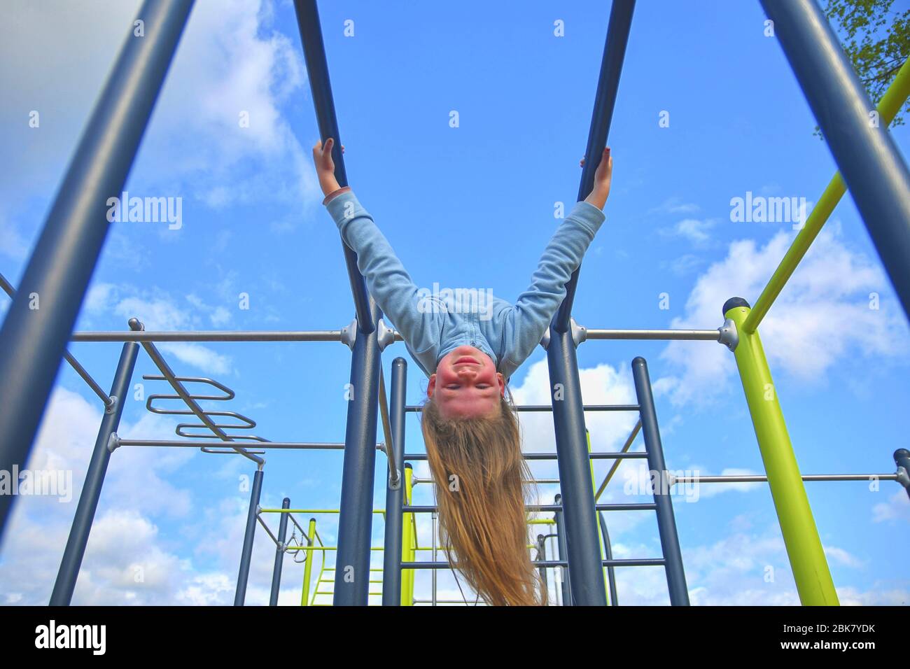 Kleines Mädchen, das kopfüber auf parallelen Bars am Spielplatz hängt. Stockfoto