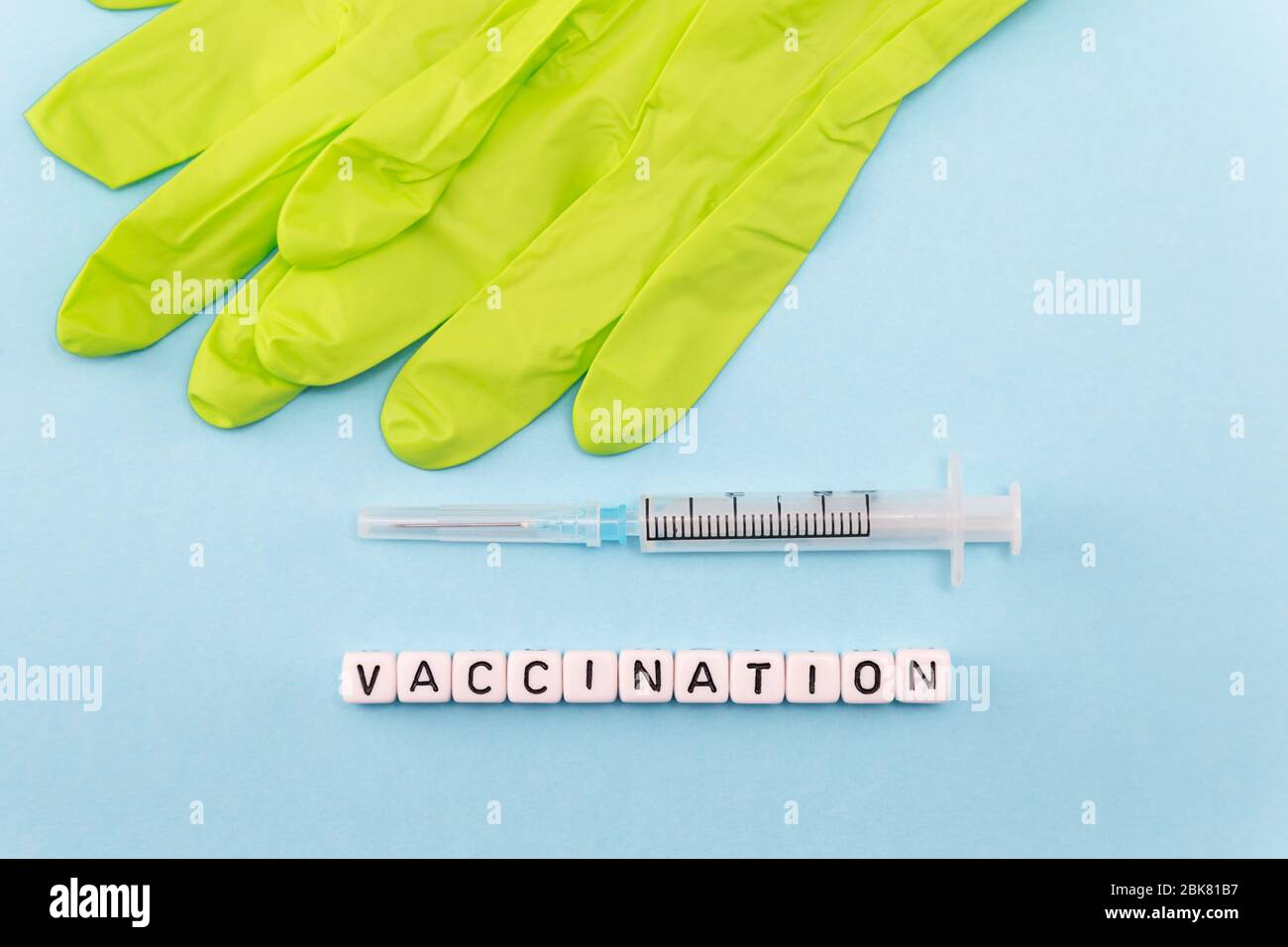 Medizinische Handschuhe, Spritze und das Wort Impfung mit Würfeln auf blauem Hintergrund Stockfoto