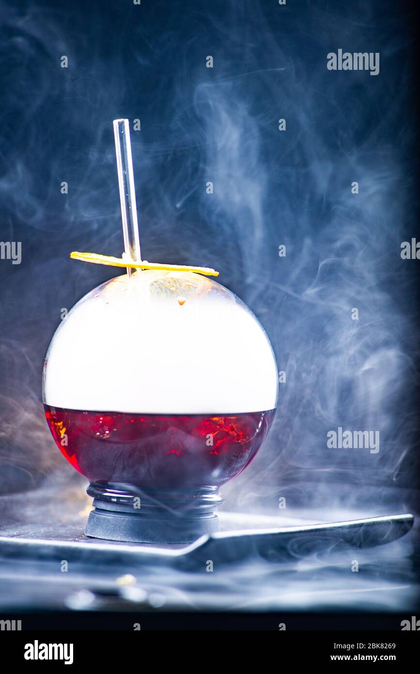 Kugelglas mit Rauch und Alkohol. Karamellisierte Zitronenscheiben. Rauch auf schwarzem Hintergrund. Stockfoto