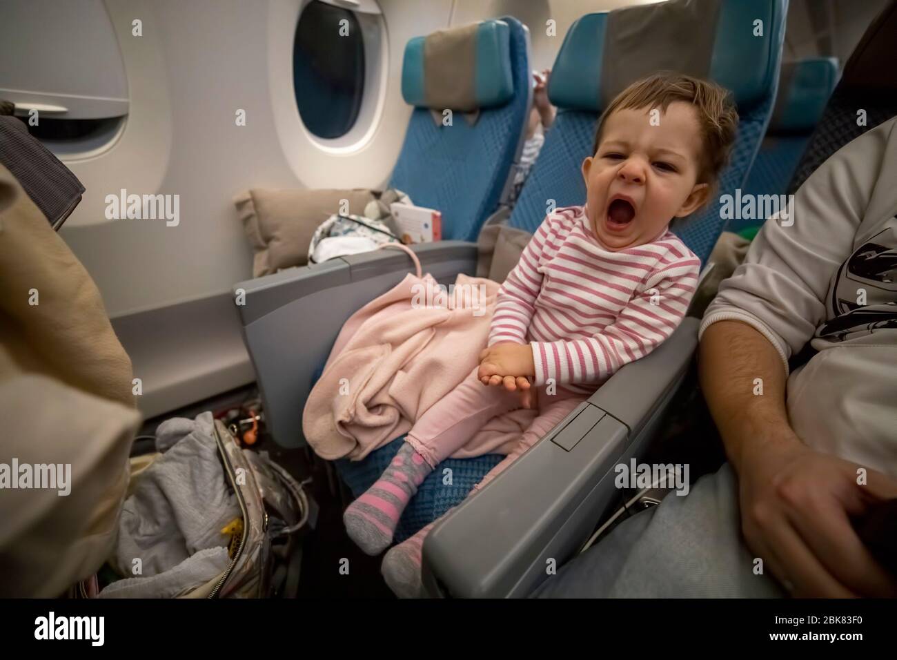 Kleines süßes, schläfriges Kleinkind, das in einem Flugzeugsitz sitzt und müde gähnt. Stockfoto