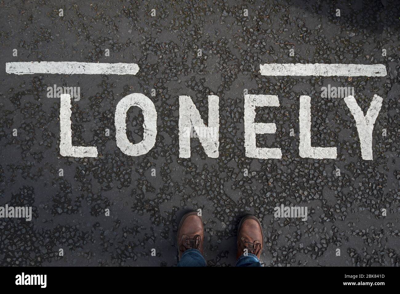 Straßenmarkierung mit dem Wort 'Lonely' und den Füßen des männlichen Fotografen. Konzept Einsamkeit. Stockfoto