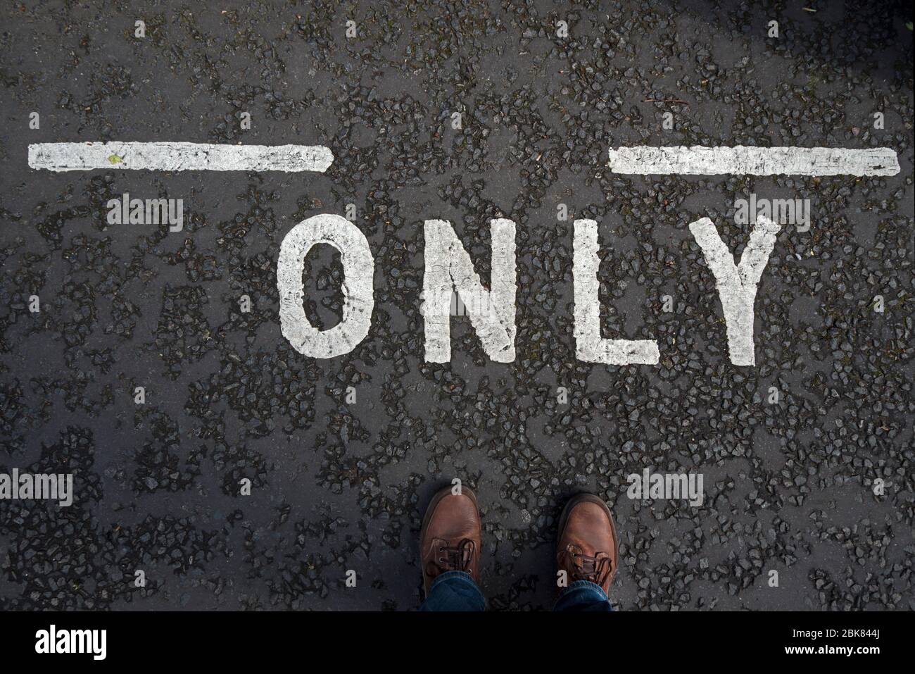 Straßenmarkierung mit dem Wort "nur" und den Füßen des männlichen Fotografen. Konzept Einsamkeit, allein. Stockfoto