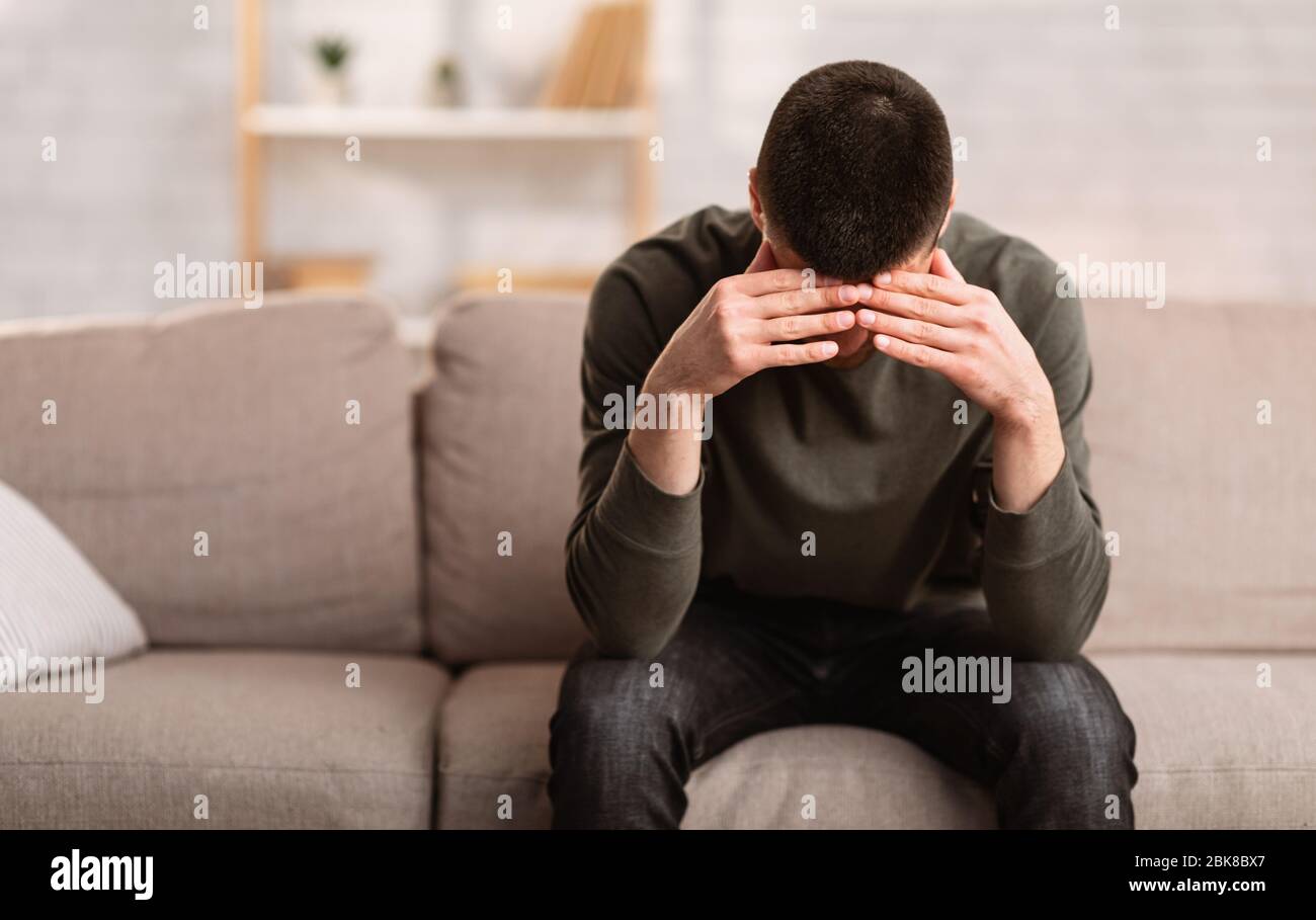 Besorgter Mann, der auf dem Sofa sitzt und den Kopf auf den Händen hält Stockfoto