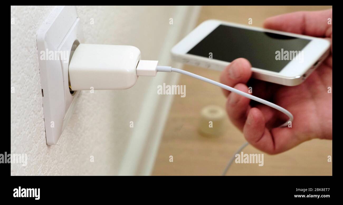 Putin weiß Smartphone auf Ladung. Verbindungskabel zum Telefon. Nahaufnahme. Stockfoto