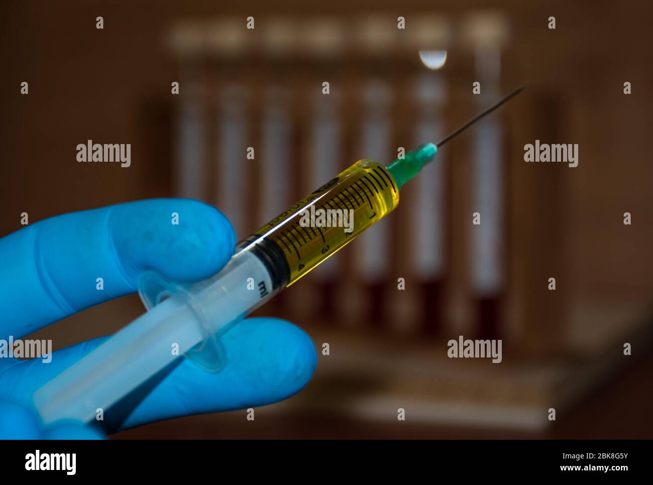 Der flüssige medizinische Impfstoff befindet sich in einem Injektor, der von einem Wissenschaftler mit einem blauen Einweghandschuh gehalten wird Stockfoto