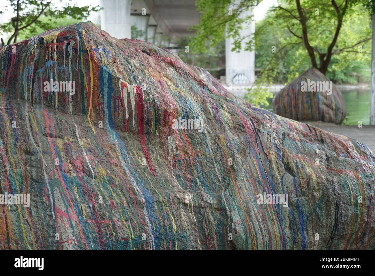 Ein großer Stein am Flussufer bedeckt Farbe ganz mit dünnen Streifen in verschiedenen Farben. Eine abstrakte Dekoration eines freistehenden Felsens. Stockfoto