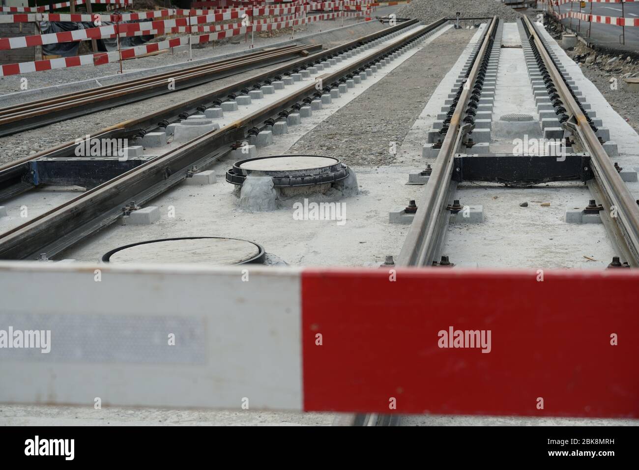 Bau einer Strassenbahnlinie, Einbettung von Metallschienen in einen Betonsockel mit einer Barrieresteele im Vordergrund und an der Seite. Stockfoto