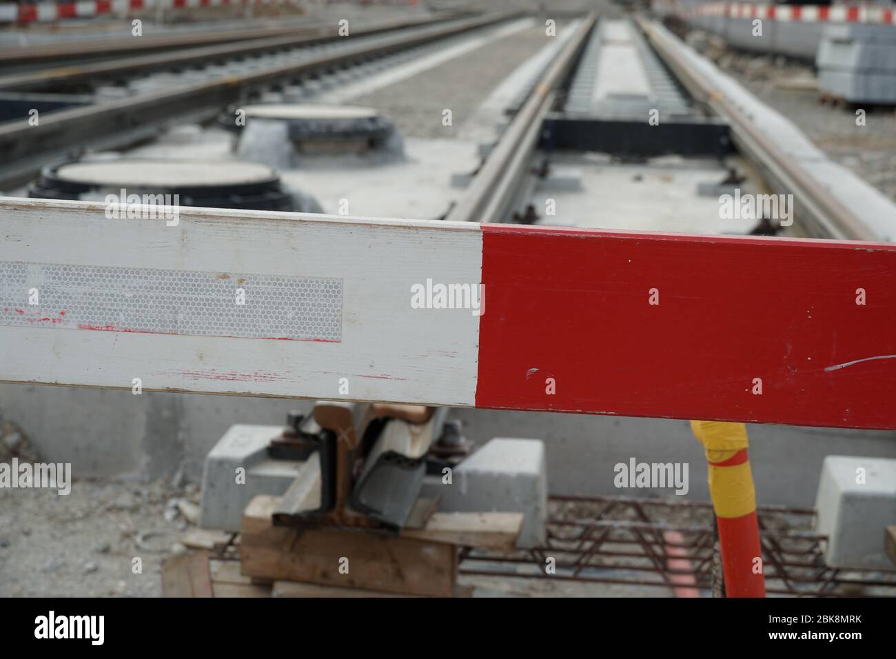 Bau einer Straßenbahn, Einbettung von Metallschienen in einen Betonsockel mit einer Barrieresteele im Vordergrund aus Sicherheitsgründen. Stockfoto