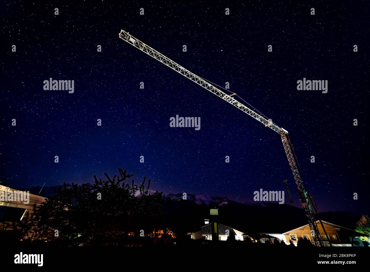 Kran über Häuser in der dunklen wolkenlosen Nacht mit Sternen mit Schneebergen Stockfoto