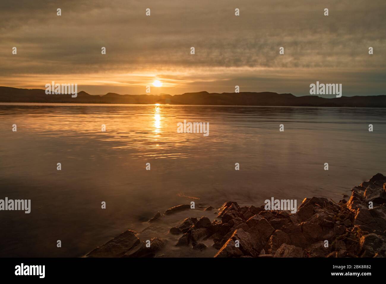 Die Sonne, die über einem See aufgeht, mit den Farben des Sonnenaufgangs, die von den Wolken und dem Wasser am Lake Pleasant in Arizona reflektiert werden. Stockfoto