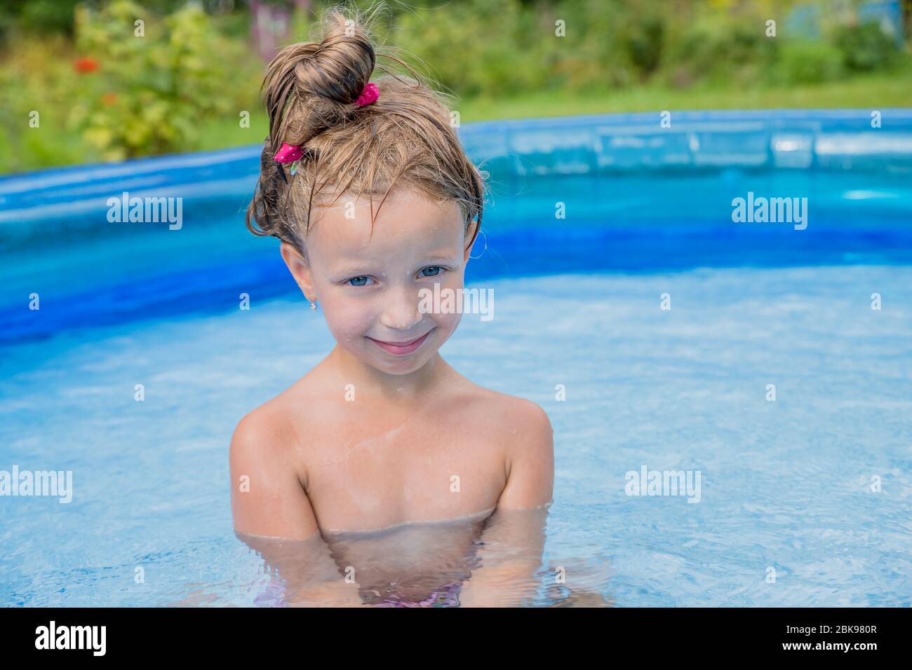 Kleines Mädchen in einem Schwimmbad in einem Sommergarten. Aufblasbares Baby-Pool. Kinder können im farbenfrohen Spielzentrum im Garten schwimmen und planschen. Happy Little Stockfoto