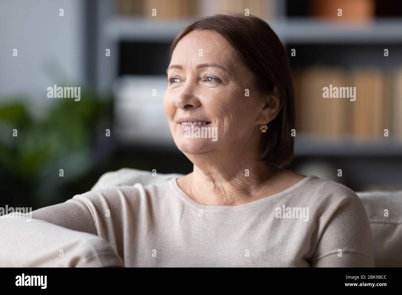 Verträumt lächelnde Frau mittleren Alters, die über gute Zukunft denkt Stockfoto