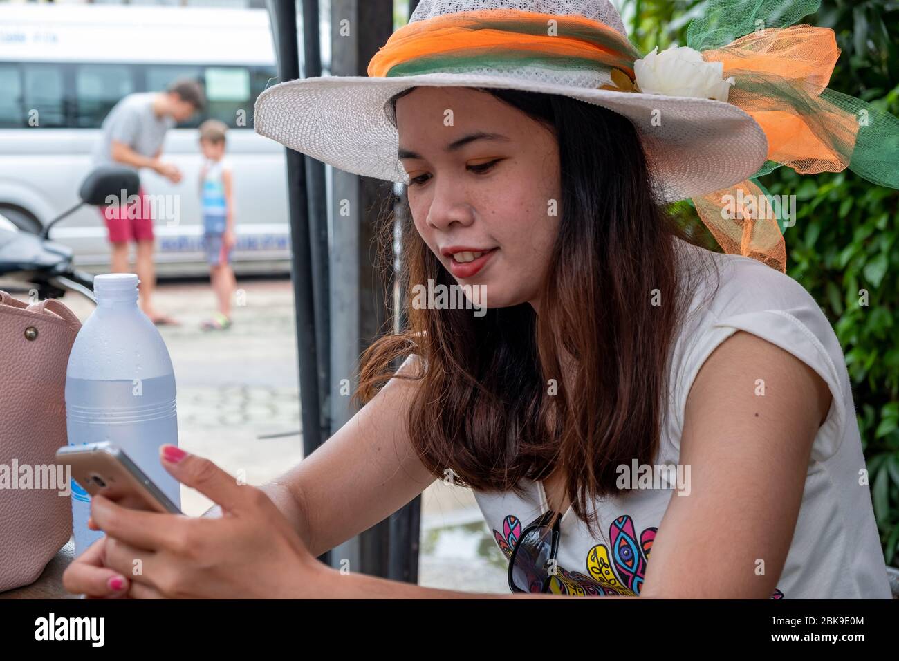 Thai Dame sitzt in einem Café und schaut lächelnd auf ihr Telefon. Stockfoto