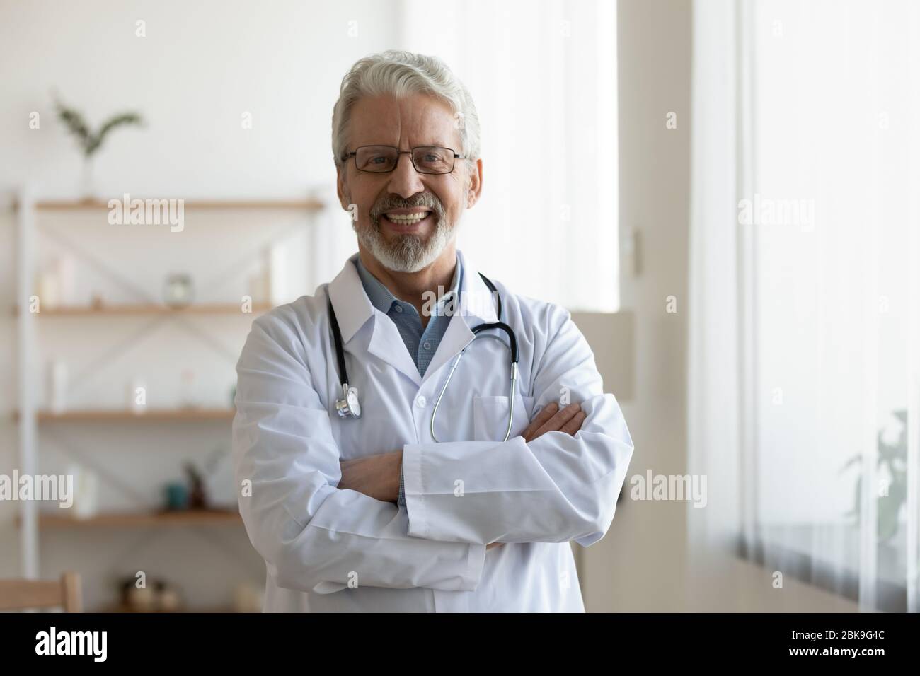 Glücklich alt professionellen Arzt stehend Arme gekreuzt Blick auf Kamera Stockfoto
