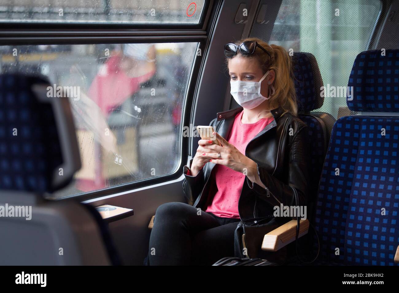 Frau mit Gesichtsmaske, in Zug sitzend, auf ihrem Handy, Corona-Krise, Stuttgart, Baden-Württemberg, Deutschland Stockfoto