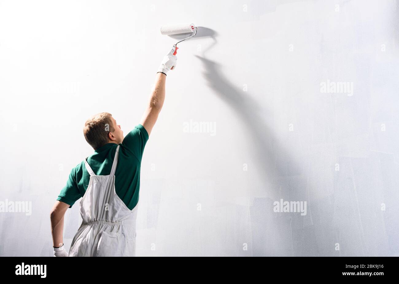 Männlicher Dekorateur, der eine Wand mit weißer Farbe malt. Stockfoto