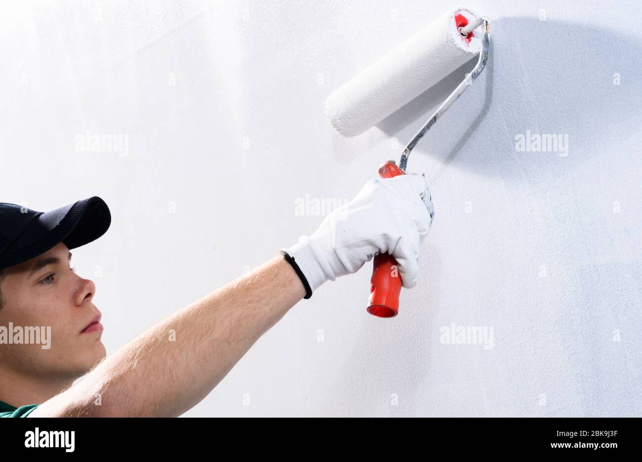 Männlicher Dekorateur, der eine Wand mit weißer Farbe malt. Stockfoto