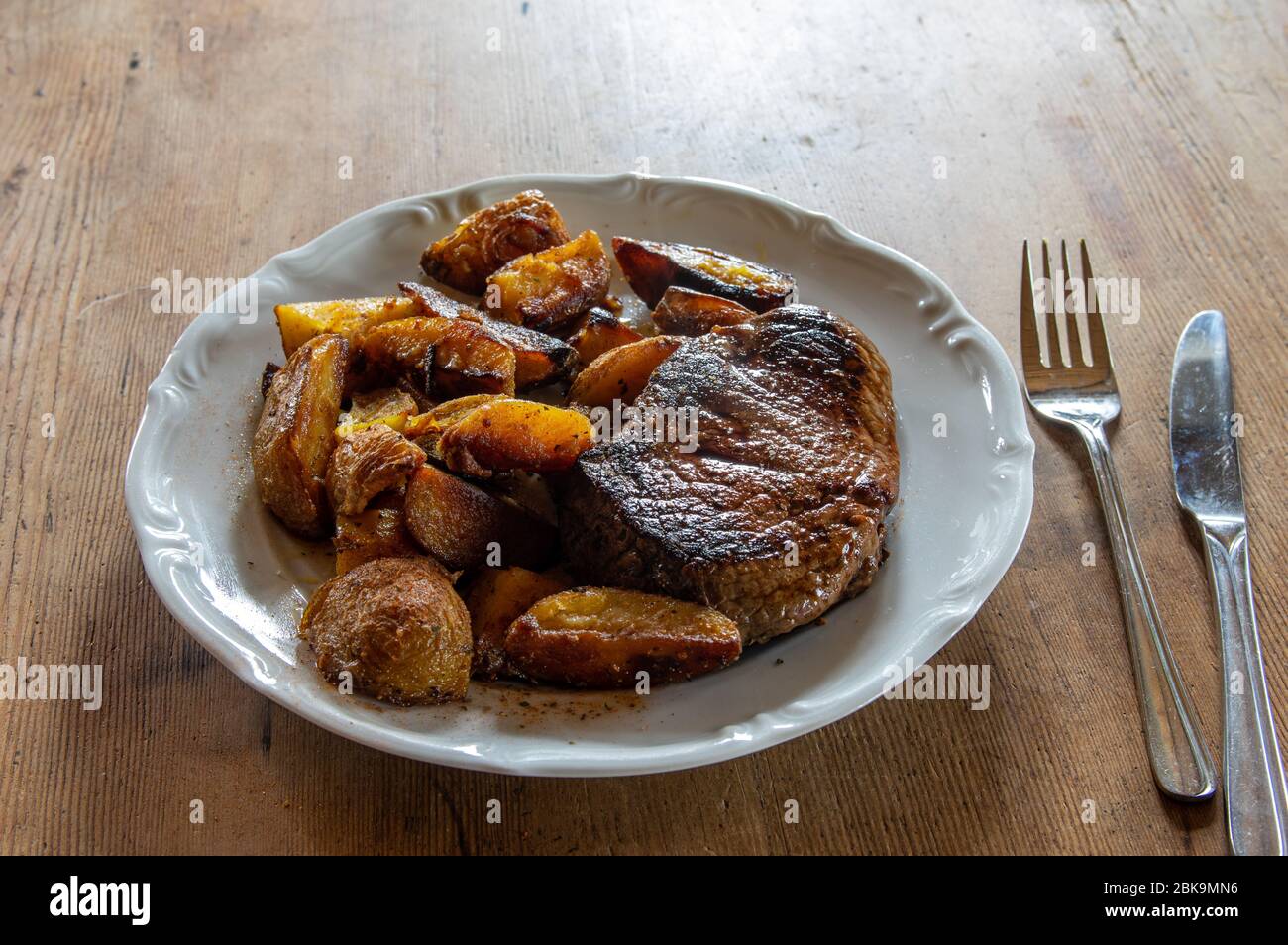 Sirloin Steak von Black Angus Rindfleisch mit Kartoffelkeilen auf einem weißen Teller auf dunklem Holztisch mit Gabel und Messer Stockfoto