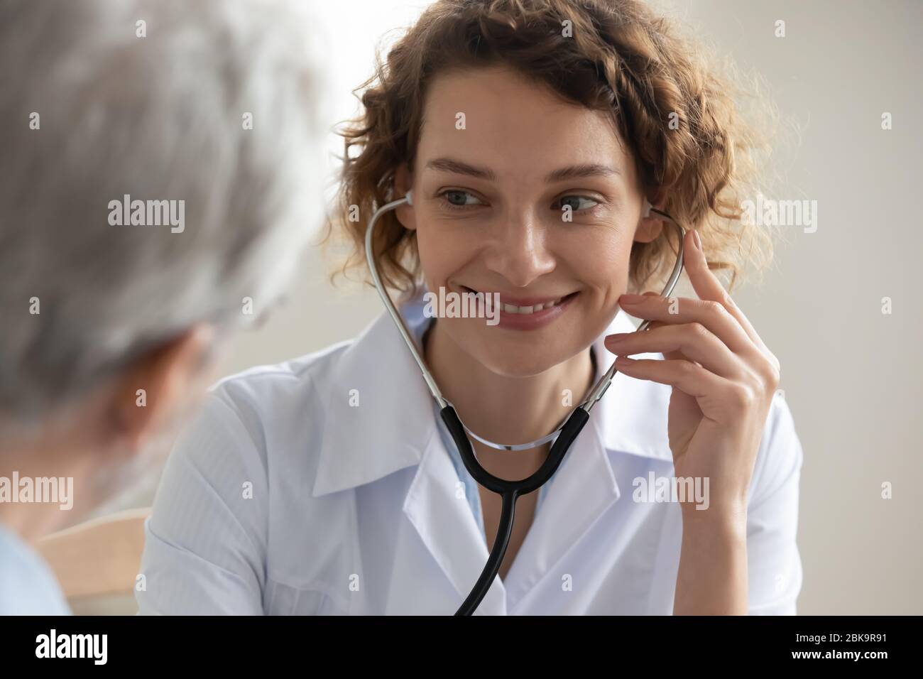 Lächelnde Ärztin mit Stethoskop hören Senior Patientin im Krankenhaus Stockfoto