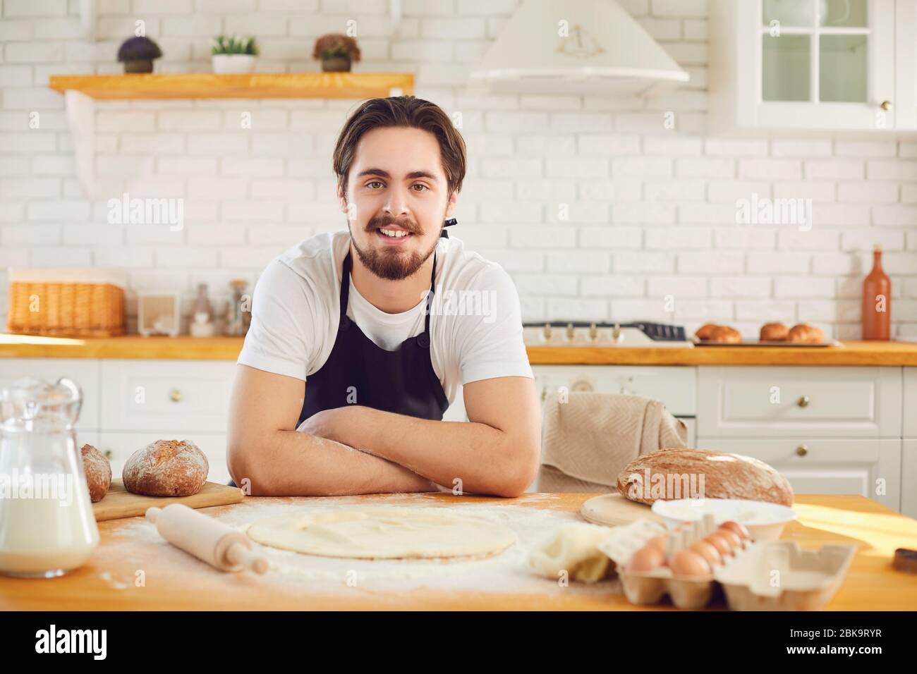 Bärtiger bärtiger Mann, der vor dem Hintergrund von frischem Brot in der Backküche lächelte Stockfoto