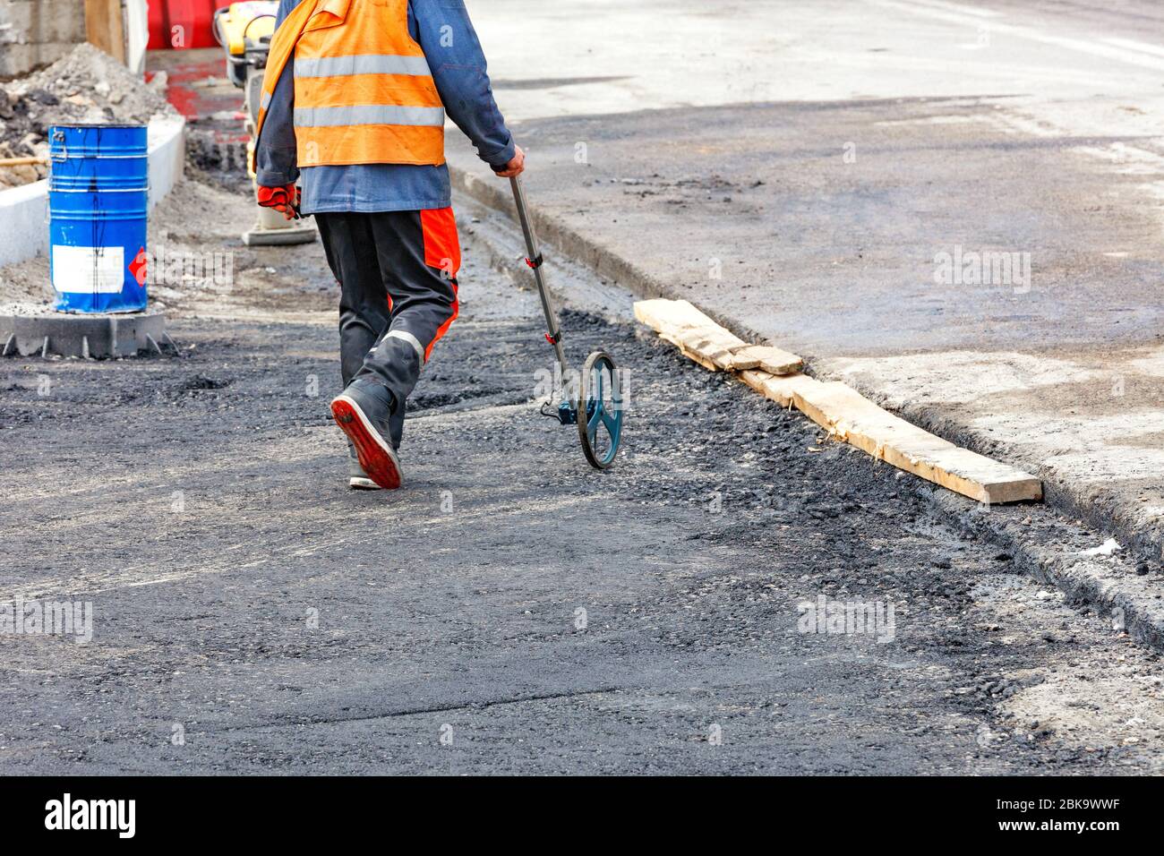 Ein Ingenieur, der die Straßenabstände mit einem Messrad misst, bestimmt die erforderliche Menge an Asphalt für die Verlegung auf einem neuen Abschnitt der Straße. Stockfoto