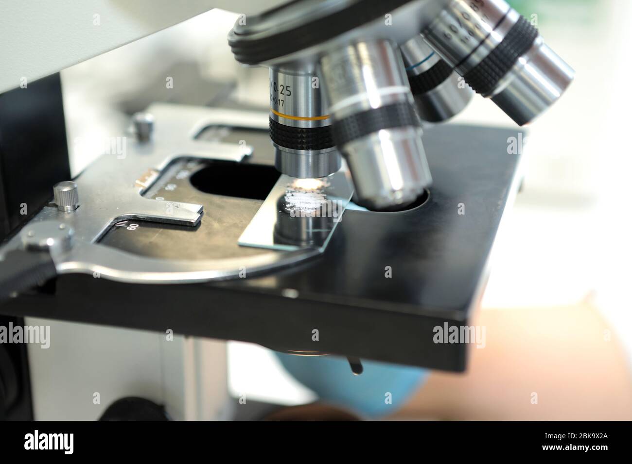 Eine Frau und ein Mann untersuchen die Struktur der Medikamentenpellets unter dem Mikroskop. Die Qualität des Pulvers der Suspension bei Vergrößerung der unde Stockfoto
