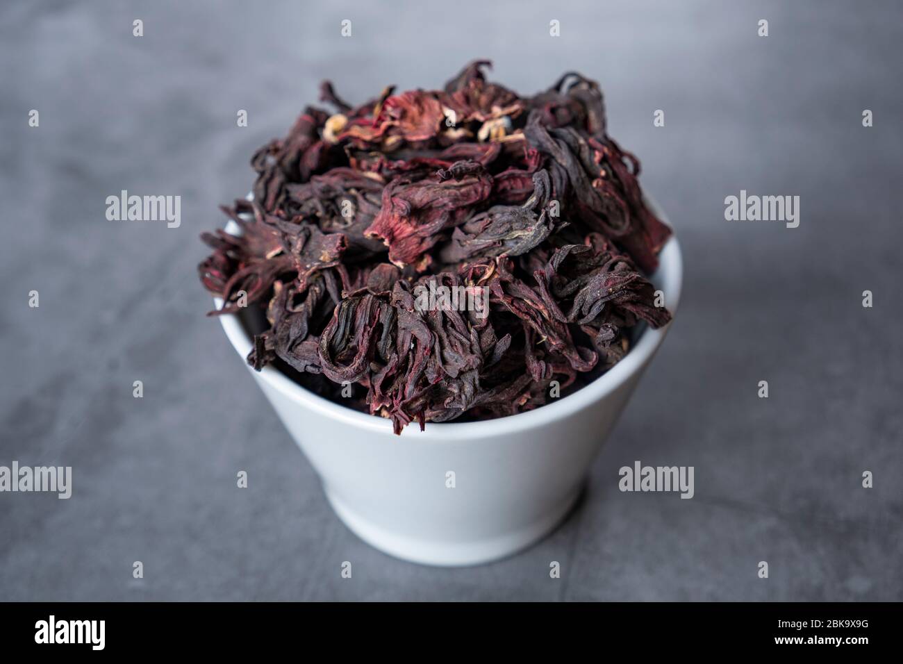 Hibiscus Tee in weißer Porzellanschale auf Stein, Betonuntergrund. Trockene, biologische, gesunde und entspannende Kräuter. Stockfoto