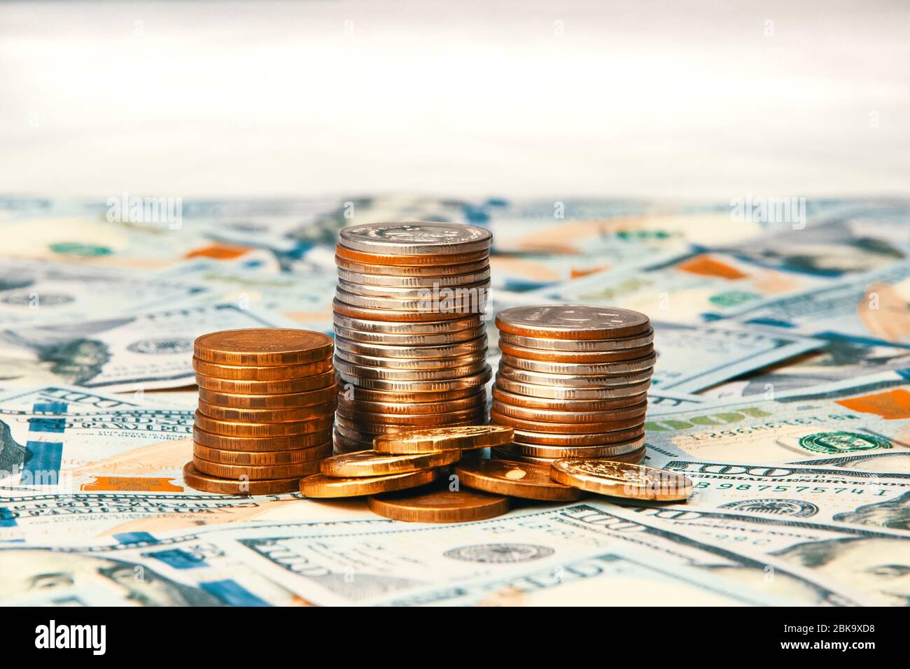 Stapel von Münzen vor dem Hintergrund von hundert-Dollar-Scheinen verstreut im Raum. Die Münzen sind in drei Spalten gesammelt, sie sind glänzend an Stockfoto