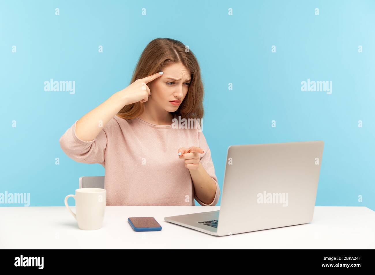 Ihr seid Idiot! Wütende Frau am Arbeitsplatz macht dumme Geste und zeigt auf Laptop-Bildschirm, dumme sinnlose Gespräch auf Videoanruf, beschuldigen dumm Stockfoto