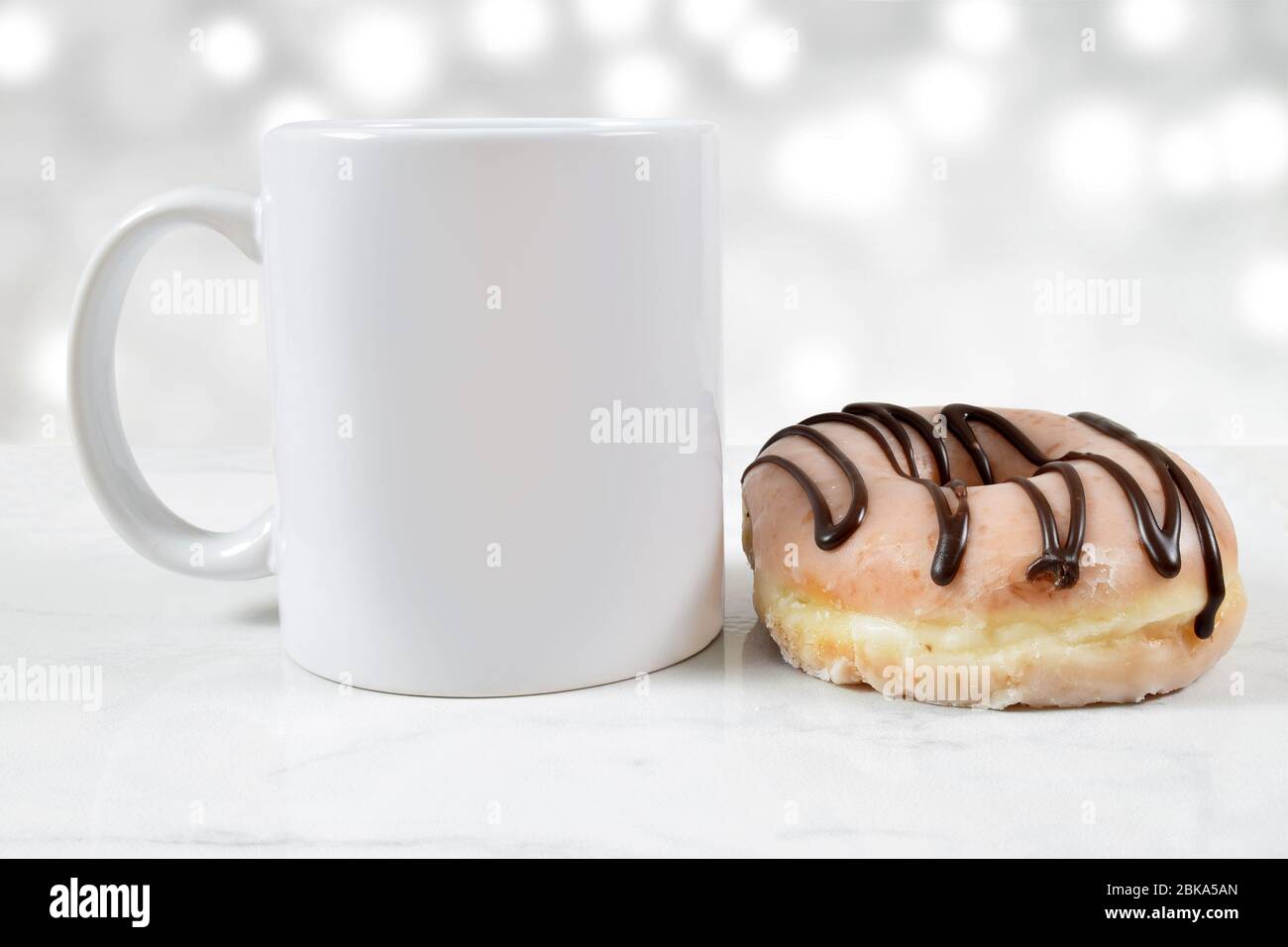 Eine 11 Unzen weiße Kaffeetasse sitzt neben einem herrlichen glasierten und Schokolade Eisdonut. Stockfoto