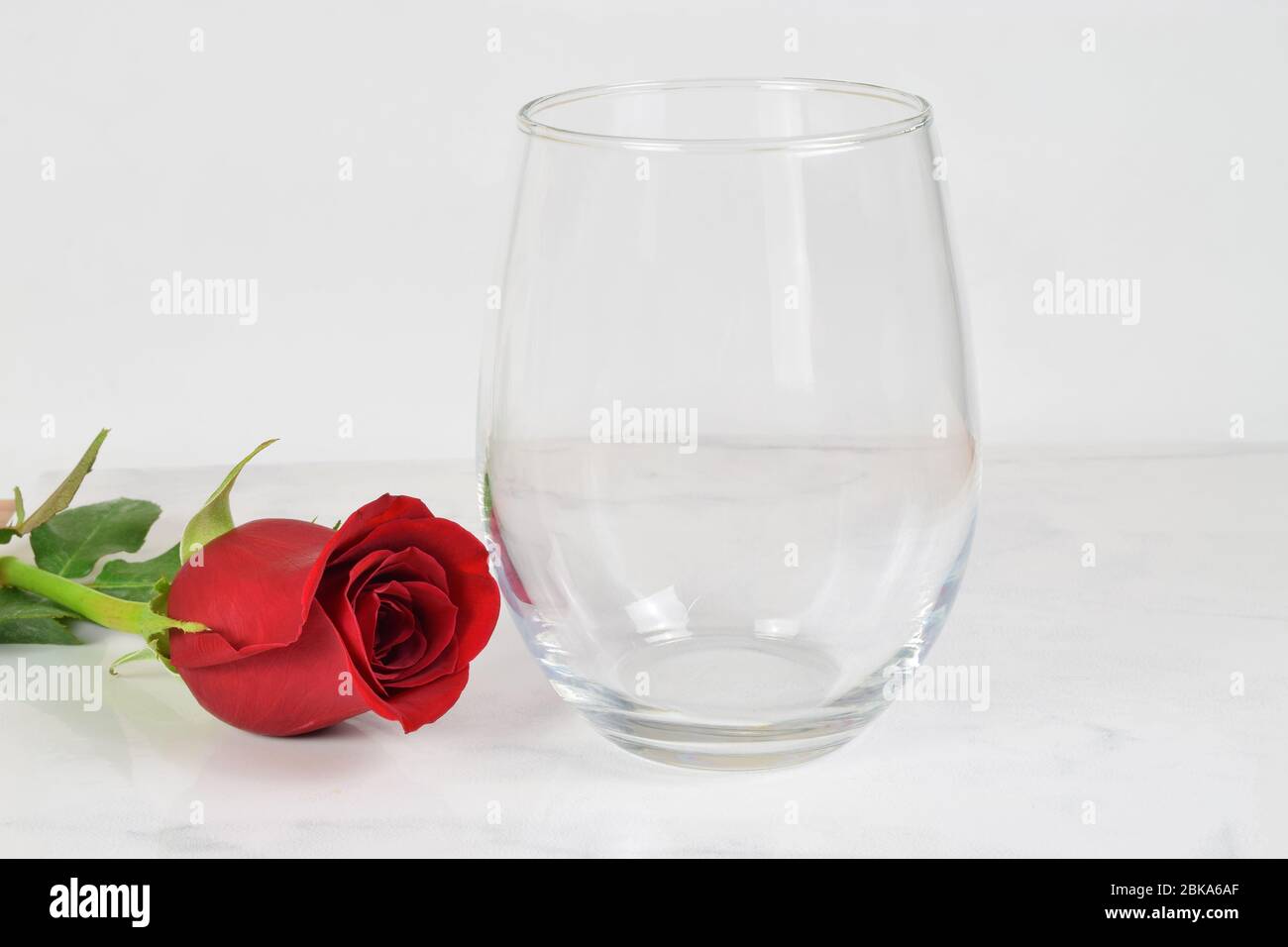 Ein No Stem Weinglas chillt romantisch neben einer langstieligen roten Rose. Stockfoto