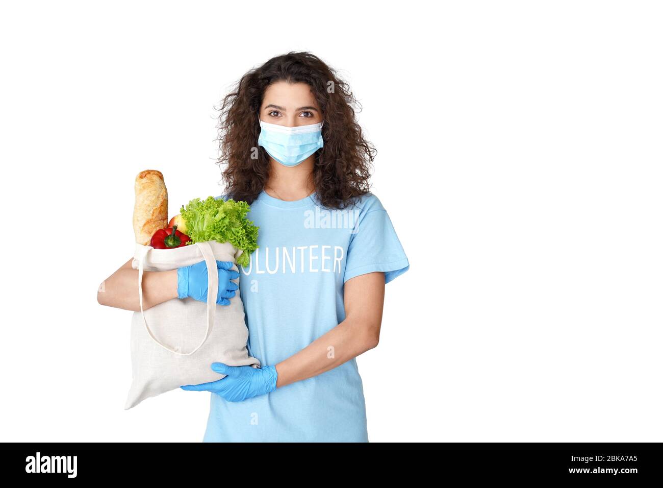 Hispanic Mädchen Volunteer tragen Maske halten Tasche mit Lebensmitteln Lieferung isoliert auf weiß. Stockfoto