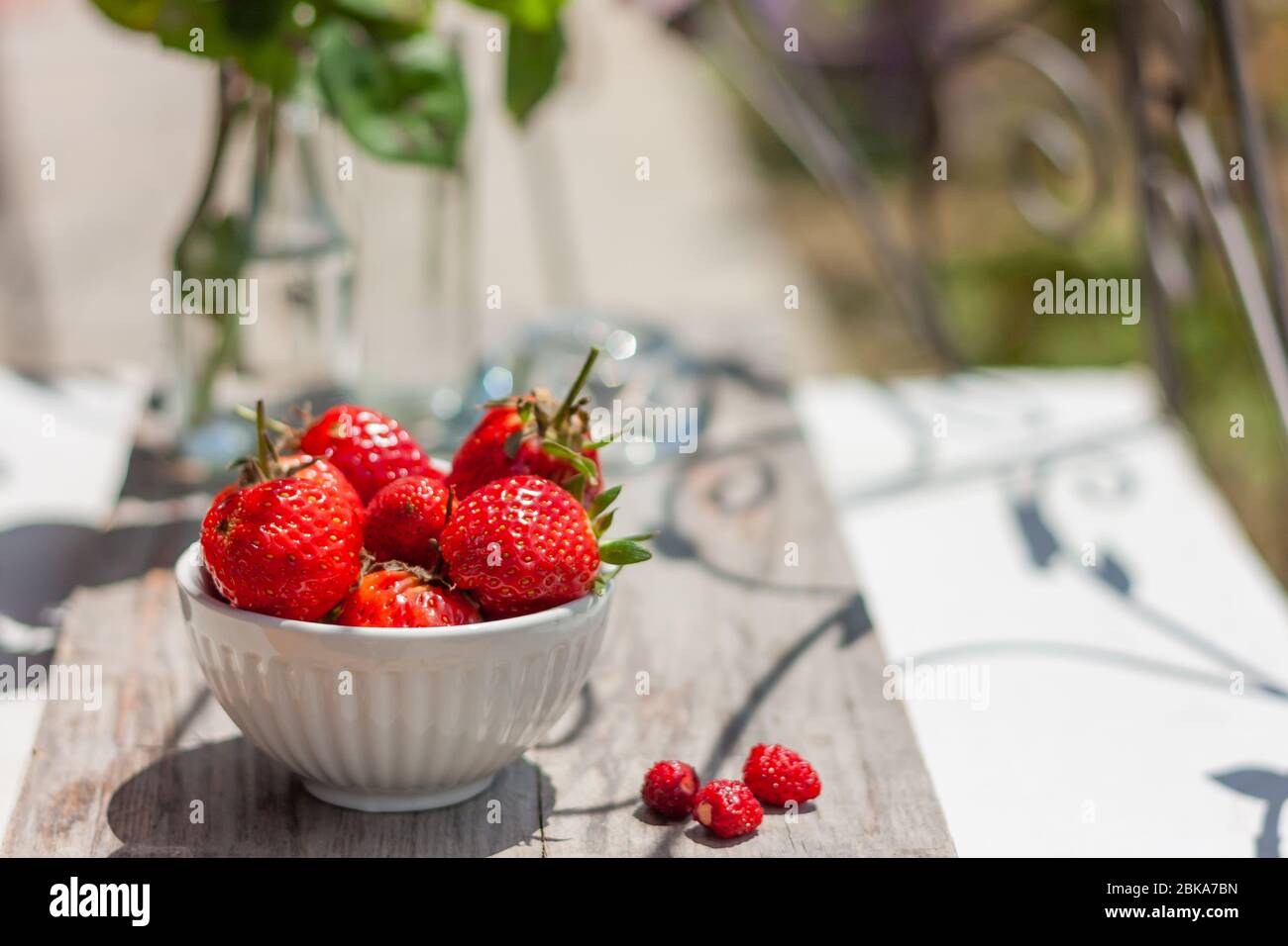 Obstschale voll mit frischen, roten, juckigen Erdbeeren auf Holztisch. Dekoration mit Blumenarrangement. Platz für Text Stockfoto