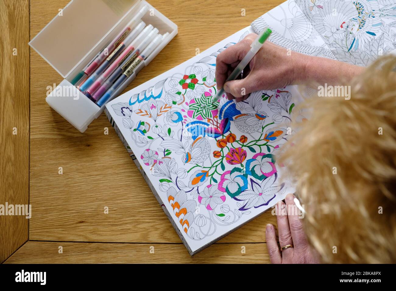 Eine reife Frau mittleren Alters Färbung in einem Erwachsenen Malbuch. Eine de streßende, beruhigende, Achtsamkeit Aktivität. Muster sind mit hellen Stiften gefärbt Stockfoto