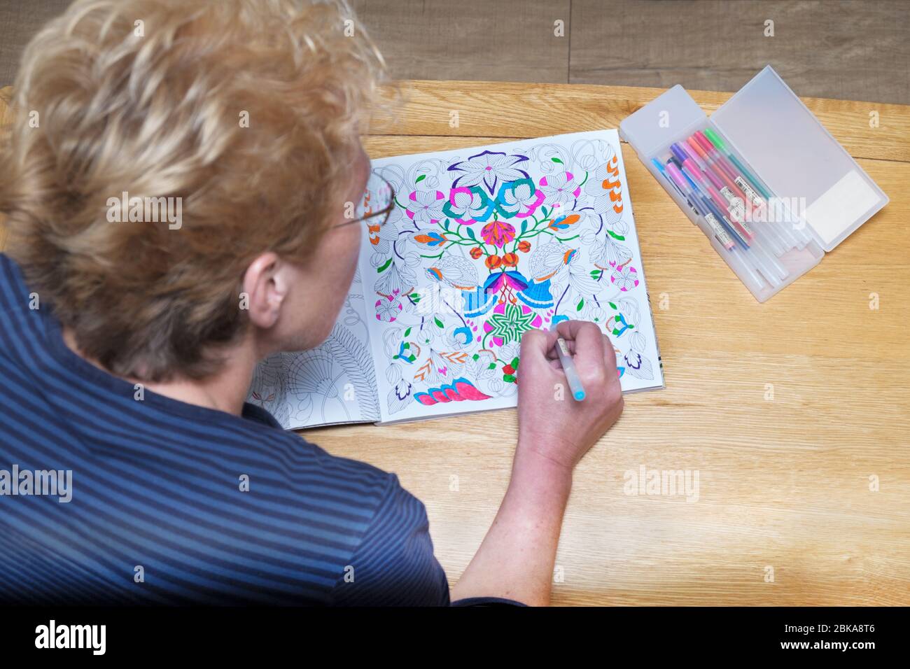 Eine reife Frau mittleren Alters Färbung in einem Erwachsenen Malbuch. Eine de streßende, beruhigende, Achtsamkeit Aktivität. Muster sind mit hellen Stiften gefärbt Stockfoto