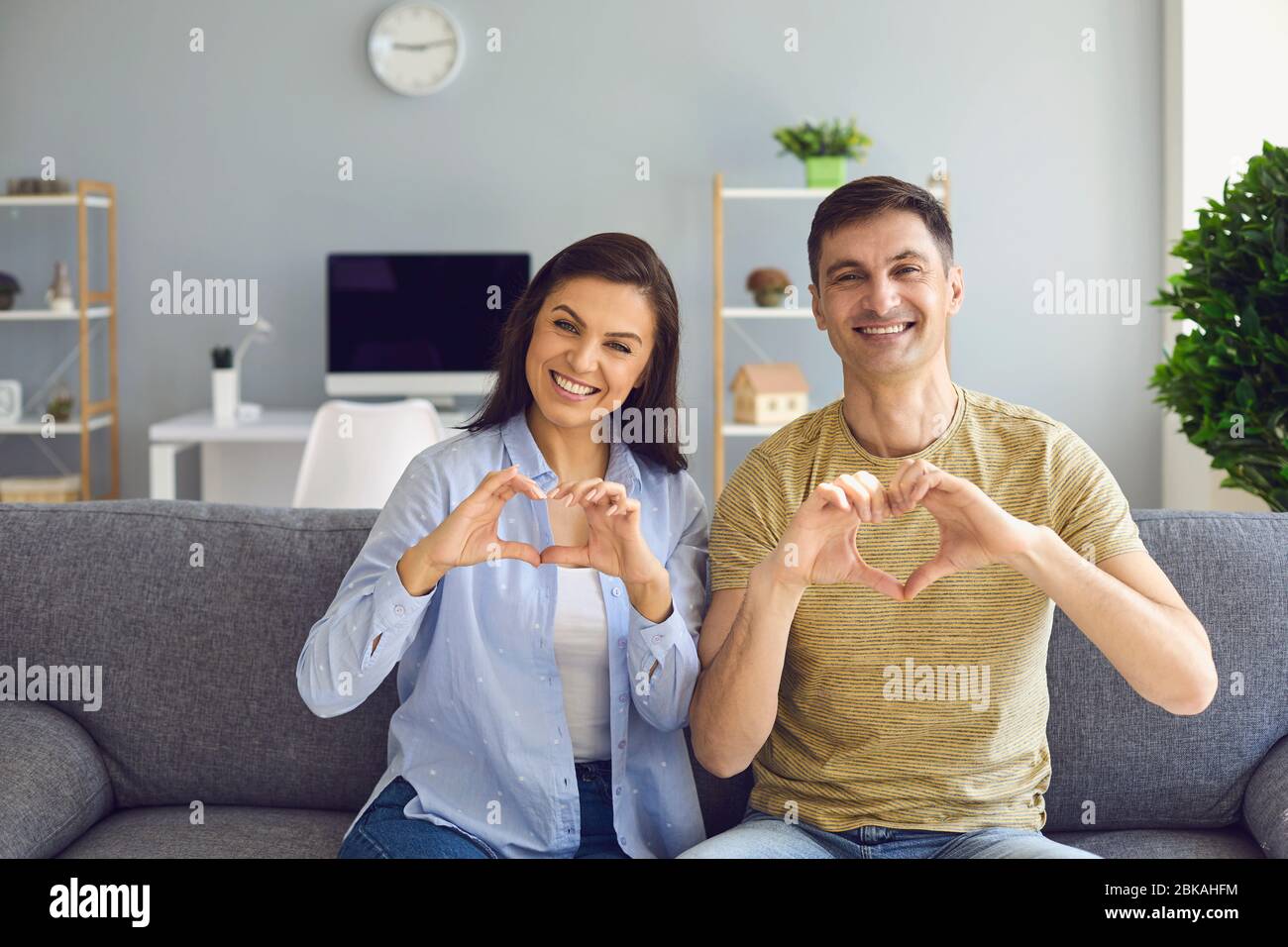 Glücklich lächelndes Paar hält die Hände in Form eines Herzens begrüßt sitzen im Haus Stockfoto