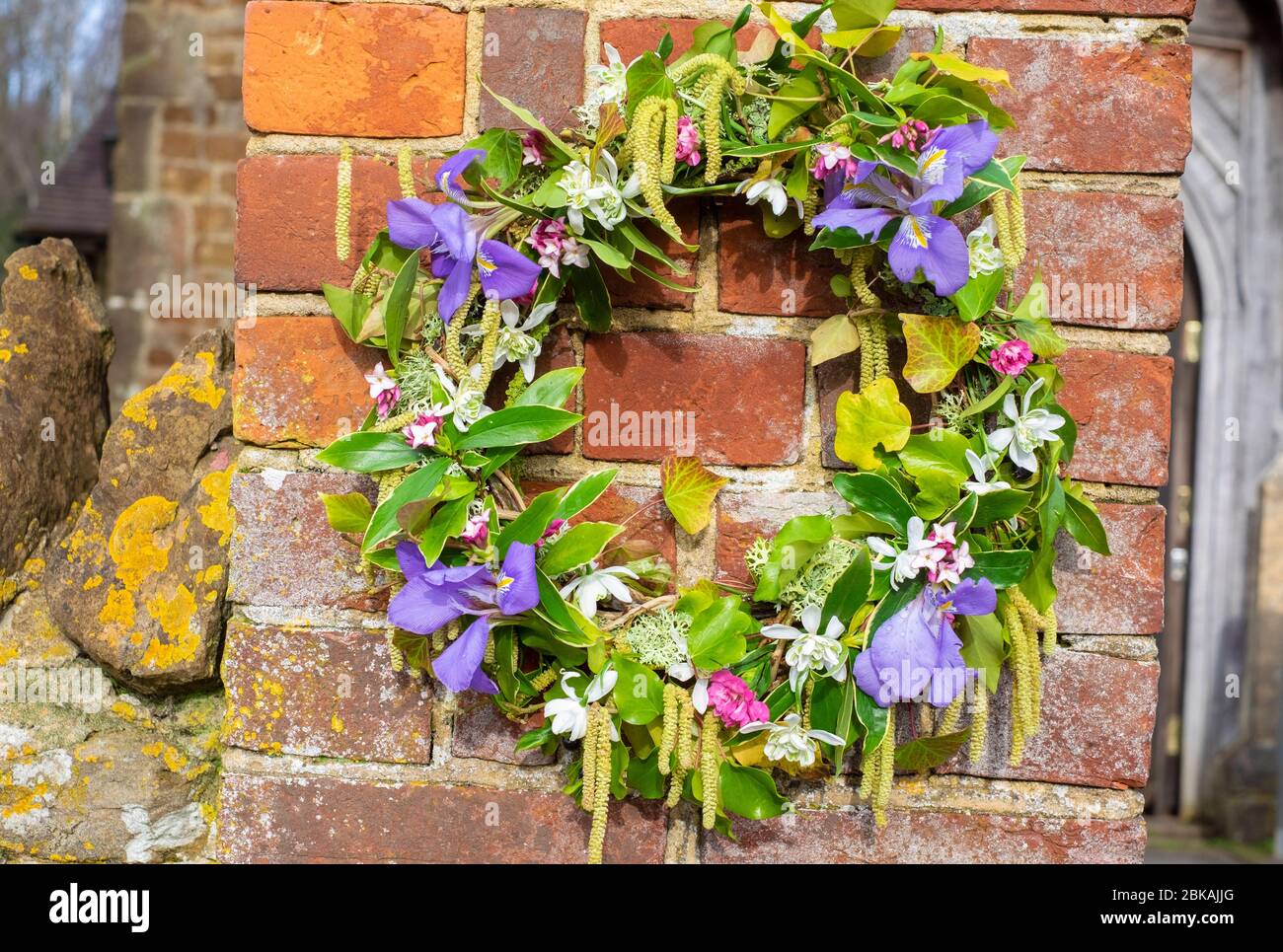 Beerdigung in einer ländlichen Kirche in Süd-Großbritannien, Kranz mit frischen Frühlingsblumen, süße daphne, Haselnuss-Kätzchen, rosa, Schneeglöckchen, Efeu, Moos, Frühling Iris Stockfoto