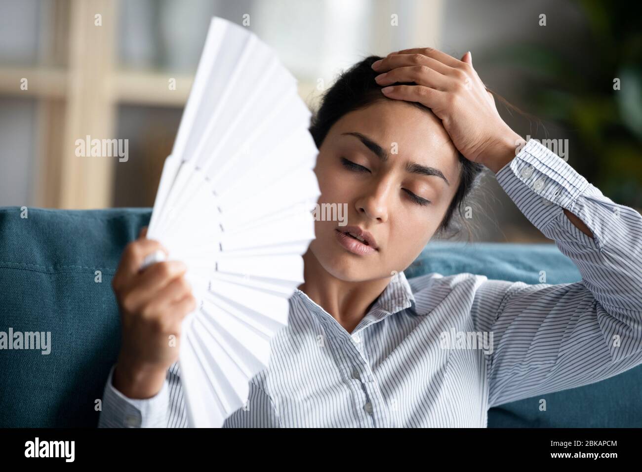 Überhitzte junge indische Frau kühlt sich mit Papierfächerpapier. Stockfoto