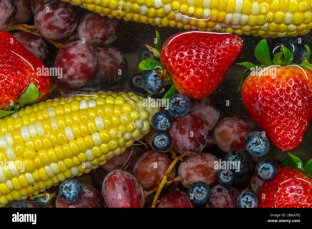 Mais, Heidelbeeren, Erdbeeren und Trauben, die im Wasser im Waschbecken schwimmen Stockfoto